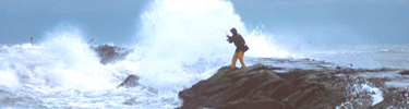 Fisherman on rock jetty in heavy waves at Isand Beach State Park.